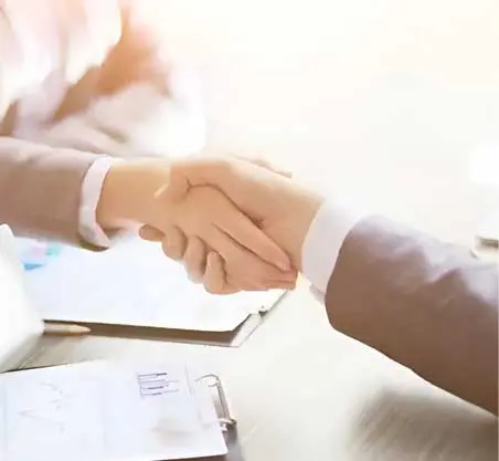 Two people shaking hands over a table.